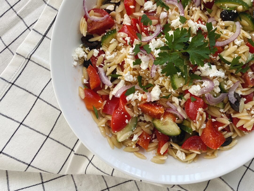 Griechischer Salat in weisser Schüssel, auf weissem Tischtuch mit schwarzem Karo-Muster