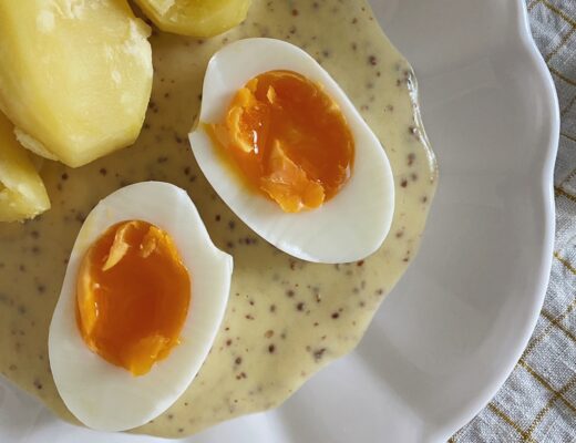 Zwei halbierte Eier auf Senfsauce mit Kartoffeln in einem weissen Teller angerichtet