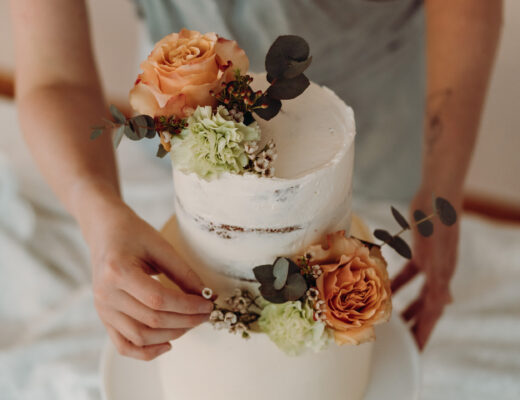 Zwei Hände wie sie eine Semi Naked Hochzeitstorte mit Frischblumen dekorieren