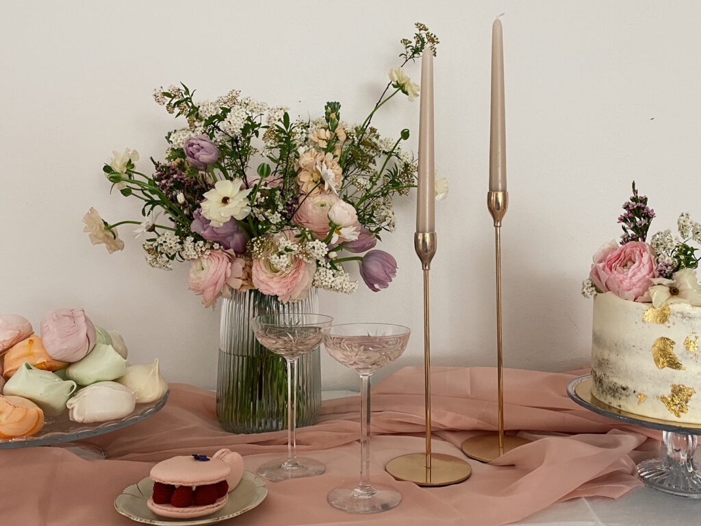 Ein Sweet Table in Pastell-Farben, angerichtet auf einem rosafarbenen Tuch, mit Kerzenhaltern und grossem Blumen-Bouquet
