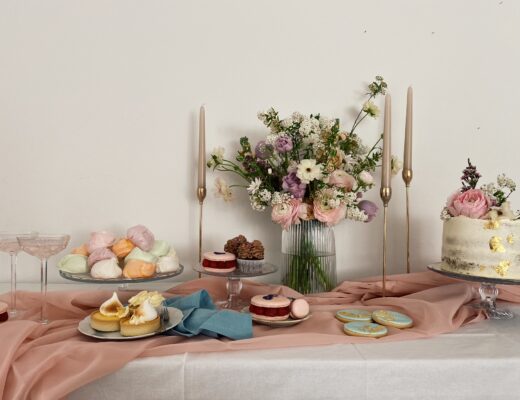 Ein Sweet Table in Pastell-Farben, angerichtet auf einem rosafarbenen Tuch, mit Kerzenhaltern und grossem Blumen-Bouquet